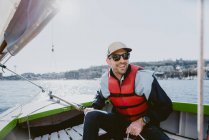 Ein hübscher junger Mann lächelt und segelt an einem sonnigen Tag mit einem kleinen Boot — Stockfoto