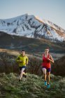 A woman and man trail run at sunset with snowy peak in the distance — Stock Photo