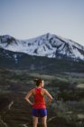 Jovem mulher olha para as montanhas enquanto trilha correndo ao amanhecer — Fotografia de Stock