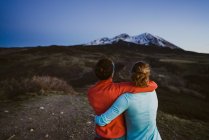 Two female friends hug and look out at mountain view at dusk — Stock Photo