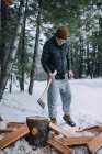 Ein Mann mit Mütze und Flanell hackt Brennholz im Schnee — Stockfoto