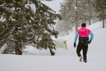 Un hombre con chaqueta brillante camina a través de la nieve profunda de su tienda - foto de stock