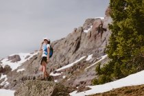 Woman trail runner sips water in front of pine trees snow and rocks — Stock Photo