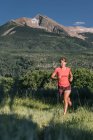 Athlétique femme sentier court à travers champ herbeux avec vue sur la montagne épique — Photo de stock