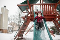 Rapaz feliz 3-4 anos desliza para baixo slide no inverno — Fotografia de Stock