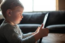 Молодий хлопчик 3-4 роки дивиться планшет у вітальні вдома — стокове фото