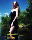 Retrato de una joven vestida de negro parada en el río - foto de stock