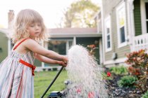 Маленькая девочка поливает растения на заднем дворе — стоковое фото