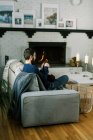 Millennial hombre ganchillo en su sala de estar por el fuego cálido y acogedor - foto de stock