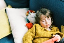 Маленька дівчинка в первинних кольорах спить на дивані з планшетом — стокове фото