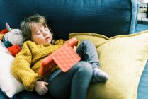 Menina criança em cores primárias dormindo no sofá com tablet — Fotografia de Stock