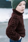 Kleiner Junge mit Hut im hausgemachten Pullover steht draußen im Schnee — Stockfoto