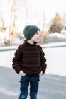 Маленький мальчик в шляпе в домашнем свитере стоит снаружи в снегу — стоковое фото
