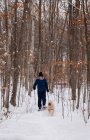 Ragazzo adolescente ciaspolata con cane nei boschi in una giornata invernale innevata. — Foto stock