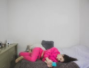 Молодая девушка лежит на диване со смартфоном — стоковое фото