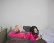 Молодая девушка лежит на диване со смартфоном — стоковое фото