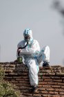 Un homme en costume de virus EPI et un masque à gaz sur son visage avec la ville en arrière-plan — Photo de stock