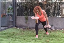 Молода жінка робить вправи з гантелями в парку — стокове фото
