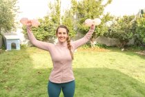 Молодая женщина делает упражнения с гантелями в парке — стоковое фото