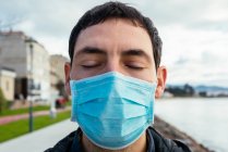 Young man on the street wearing a face mask with eyes closed — Stock Photo
