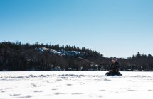 Menino pesca enquanto sentado na neve — Fotografia de Stock