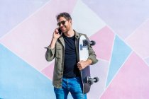 Junger Mann mit Skateboard spricht vom Smartphone — Stockfoto