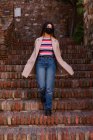 Натуральна молода жінка з маскою спускається сходами старого міського будівництва — стокове фото