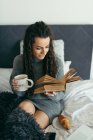 Woman reading a book with tea on a white couch. — Stock Photo