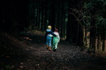 Les enfants marchant les bras les uns autour des autres dans la forêt sombre — Photo de stock