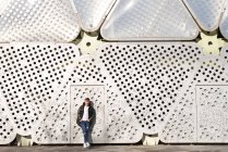 Молодой человек с руками на карманах стоит у металлической стены — стоковое фото