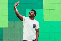 Schwarzer afroamerikanischer Junge auf grünem Hintergrund macht ein Selfie mit seinem Handy. — Stockfoto