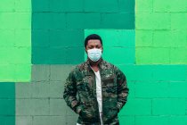Afroamerikanischer schwarzer Junge auf grünem Wandhintergrund. Bekleidet mit Militärjacke und Gesichtsmaske. — Stockfoto