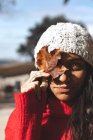 Eine schöne Frau hält im Herbst ein Blatt mit Wintermütze — Stockfoto