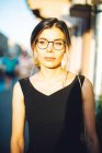 Молода жінка в чорній сукні і окулярах в сонячному місті — стокове фото