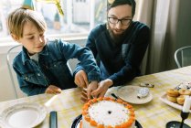 Pai e filho cortando e servindo bolo de aniversário na celebração do divertimento — Fotografia de Stock
