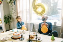Pai e filho rindo juntos enquanto brincam com balões de aniversário — Fotografia de Stock