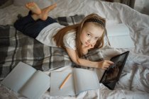 Chica acostada en la cama rodeada de cuadernos - foto de stock
