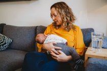 Белая блондинка мама кормит грудью новорожденного мальчика на диване дома — стоковое фото