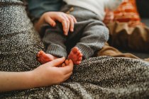 Close up of older child holding newborn baby's feet at home — Stock Photo
