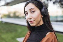 Porträt einer jungen schönen brünetten Frau mit Kopfhörern, die auf der Straße Musik hört — Stockfoto