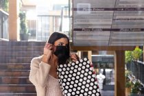 Ragazza bruna spagnola con maschera facciale che cammina con le borse della spesa in un centro commerciale. — Foto stock