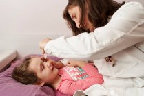 Female doctor smiling and giving eye drops to a little girl in her bed. Home doctor concept — Stock Photo
