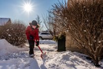 Menino de casaco vermelho limpando a neve da passarela de sua casa. — Fotografia de Stock