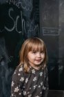 Симпатичная маленькая девочка смотрит на меня с улыбкой на лице с доской на б — стоковое фото