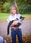 Giovane ragazza bionda che tiene un gatto in bianco e nero all'aperto — Foto stock