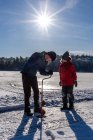 Dos chicos usando sinfín para hacer un agujero en el hielo en un día soleado de invierno. - foto de stock