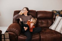 Beautiful young mother and her daughter on sofa — Stock Photo