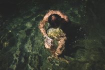 Ragazzo porta una pietra sommersa sotto l'acqua increspata — Foto stock