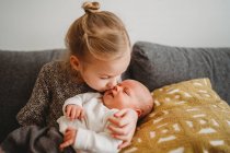 Beautiful white girl kissing newborn baby brother on the couch at home — Stock Photo