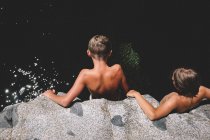 Dos chicos bronceados miran desde un acantilado hacia el río en pleno verano - foto de stock